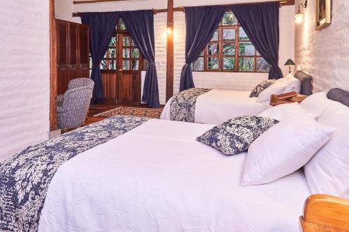 a bedroom with two beds and two windows at Boutique Hotel La Carriona in Sangolquí