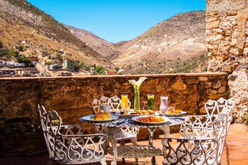 einen Tisch und Stühle auf einer Terrasse mit Bergen im Hintergrund in der Unterkunft Mesón de la Abundacia in Real de Catorce