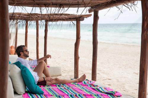 a man sitting on a couch on the beach at La Zebra Tulum, a Small Luxury Hotel in Tulum