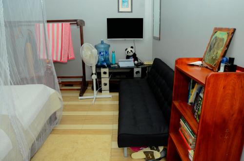 a bedroom with a couch and a desk with a tv at Alice Gardens & Campsite in Entebbe