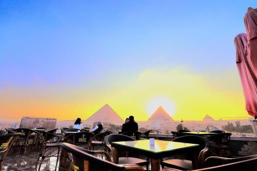 um grupo de pessoas sentadas em mesas olhando para as pirâmides em MagiC Pyramids INN em Cairo