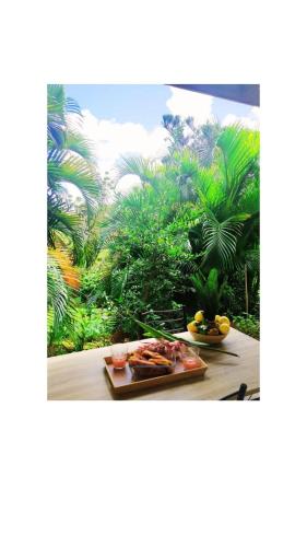 ein Teller mit Lebensmitteln auf einem Tisch mit Bäumen im Hintergrund in der Unterkunft Villa tropicale charmant T2 dans un cadre verdoyant in Gros-Morne