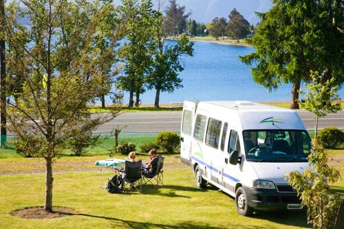 Una coppia seduta su una sedia accanto a un furgone bianco di Te Anau Lakeview Holiday Park & Motels a Te Anau