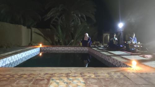 a group of people standing around a pool at night at Camp & Trek in Mhamid