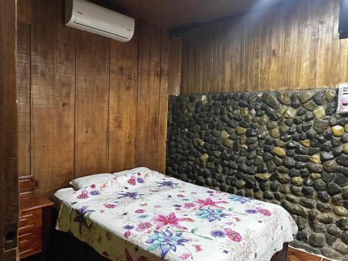 a bedroom with a bed and a stone wall at Mochileros MarAbi in Tarcoles