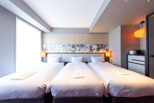 two beds in a hotel room with white sheets at Hotel Forza Kyoto Shijo Kawaramachi in Kyoto