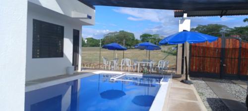 a swimming pool with blue umbrellas and a table and chairs at Quinta el Progreso in Carmen de Apicalá