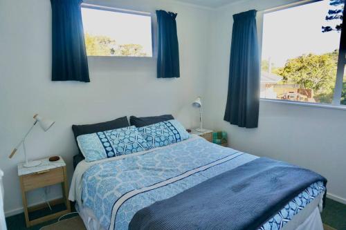 a bedroom with a bed with blue sheets and two windows at The Green Guesthouse - beautiful semi rural family unit in Lower Hutt