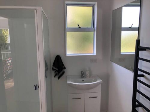 a white bathroom with a sink and two windows at The Green Guesthouse - beautiful semi rural family unit in Lower Hutt