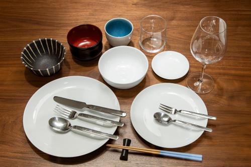 a wooden table with white plates and forks and glasses at HOTEL MASTAY jingumichi in Kyoto