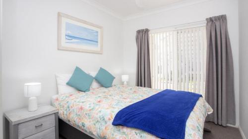 a bedroom with a bed with blue sheets and a window at Apartment 16 - The Meridian in Old Bar