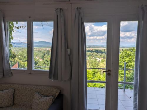 a room with two large windows and a view of the countryside at Páratlan Panoráma Kisház in Tahitótfalu