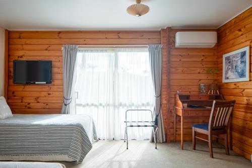 a bedroom with a bed and a window with a desk at Fox Glacier Lodge in Fox Glacier