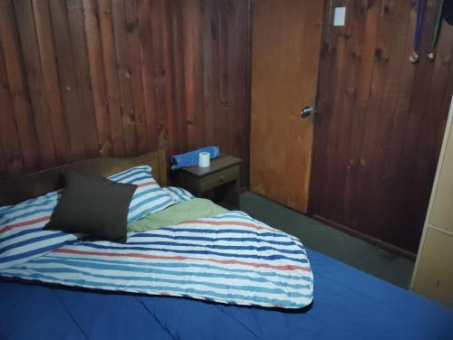 Una cama con una manta a rayas y una mesita de noche en Pensión San Andrés, en Concepción