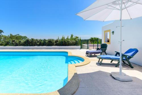 a swimming pool with an umbrella and two chairs and a table at Monte do Cerro Verde in Santiago do Cacém