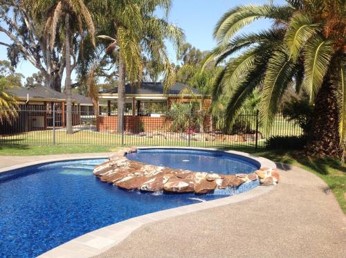 a swimming pool with lounge chairs in front of a house at Sportsmans Motor Inn in Barooga