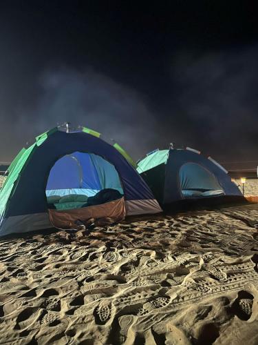two tents on a sandy beach at night at Dubai Tourism and Travel Services in Hunaywah