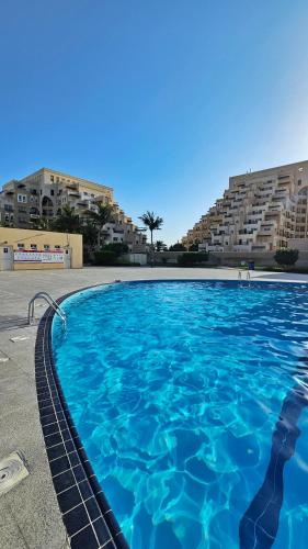a large blue swimming pool with buildings in the background at Beach Apartment in Ras al Khaimah