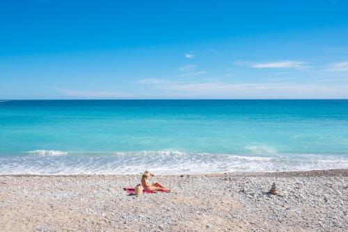 a woman sitting on a beach near the ocean at Le COQ Impérial - Parking - Spacieux in Menton