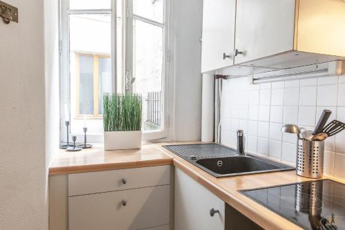 une cuisine avec des armoires blanches, un évier et une fenêtre dans l'établissement Montmartre Apartments - Degas, à Paris