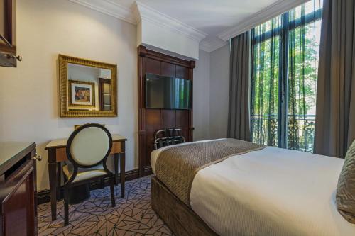 ロンドンにあるHyde Park Internationalのベッド、デスク、窓が備わるホテルルームです。
