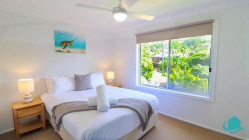 a white bedroom with a bed and a window at Oceanview Beach House in Caves Beach