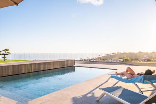 Eine Frau, die auf einem Stuhl neben einem Pool liegt. in der Unterkunft Villa Elysian Oasis by Homie in Prazeres
