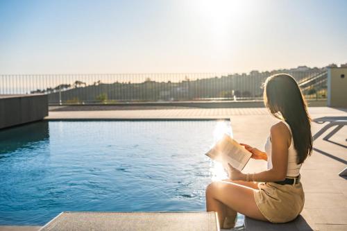 Eine Frau liest ein Buch neben einem Pool in der Unterkunft Villa Elysian Oasis by Homie in Prazeres