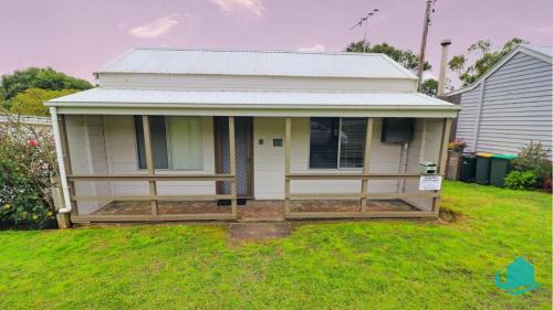 a small white house with a porch in a yard at Catho Cottage in Catherine Hill Bay