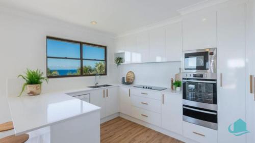 a white kitchen with white cabinets and a window at Waves at Caves in Caves Beach