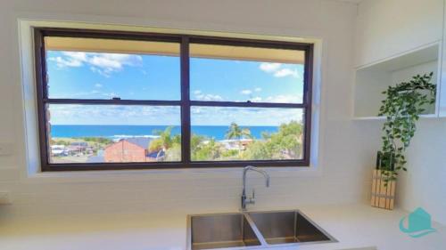 a window above a kitchen sink with a view of the ocean at Waves at Caves in Caves Beach