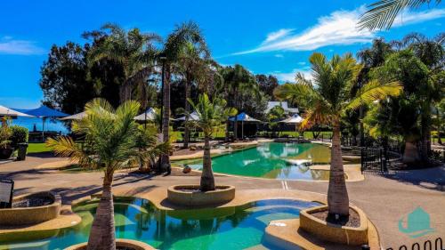 a pool with palm trees in a resort at Oystercatcher at Raffertys Resort- family villa in Cams Wharf