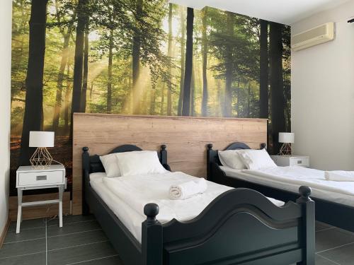 2 camas en un dormitorio con un mural forestal en MiLLER's Inn Panzió és Étterem, en Nagyoroszi