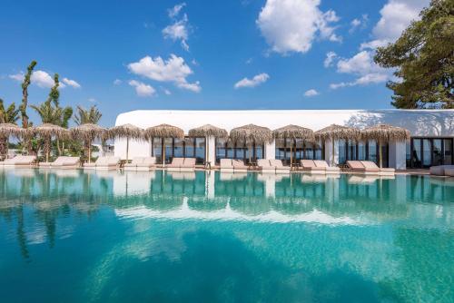 uma piscina com cadeiras e um edifício em Isla Brown Corinthia Resort & Spa, Curio Collection by Hilton em Agioi Theodoroi