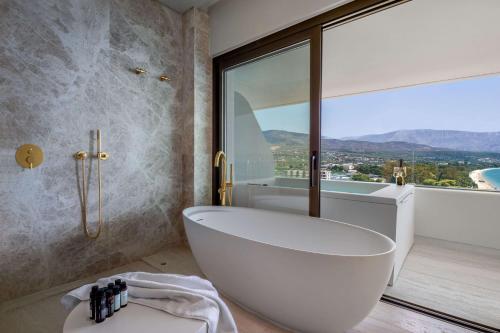 a bathroom with a tub and a large window at Isla Brown Corinthia Resort & Spa, Curio Collection by Hilton in Agioi Theodoroi