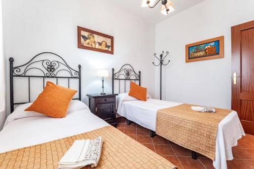 two beds in a room with white walls and orange pillows at Casa rural Montemayor in Moguer