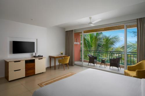 a bedroom with a bed and a television and a balcony at Mandrem Beach Resort, a member of Radisson Individuals Retreat in Mandrem
