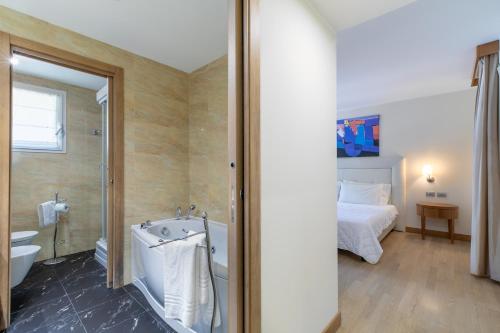 un bagno con vasca e una camera con letto di Hotel Villa Doimo a Lignano Sabbiadoro