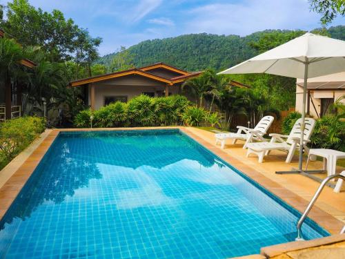 a pool with chairs and an umbrella next to a house at Escape-Cabins in Ko Lanta