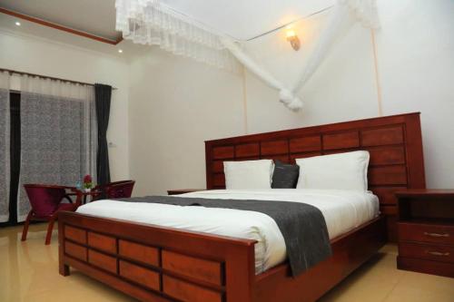 a bedroom with a large wooden bed with white sheets at Fort Breeze Hotel in Fort Portal