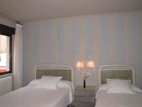 two beds in a bedroom with two lamps on the wall at Hotel Migal in Cue