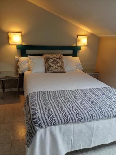 a bedroom with a large white bed with two lamps at Hotel Migal in Cue