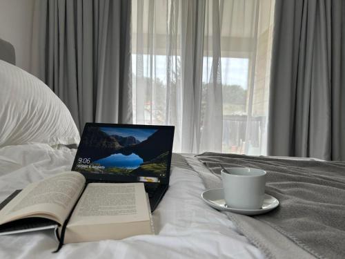 um computador portátil numa cama com um livro e uma chávena de café em CASA V Deluxe Queen Rooms em Kiseljak