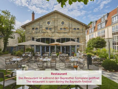 um restaurante com mesas e guarda-sóis em frente a um edifício em H4 Hotel Residenzschloss Bayreuth em Bayreuth