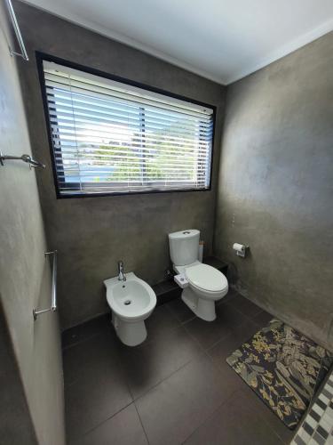 a bathroom with a toilet and a sink and a window at LA HACIENDA - MODERN, BRIGHT, STYLISH House with Private Pool in Cape Town