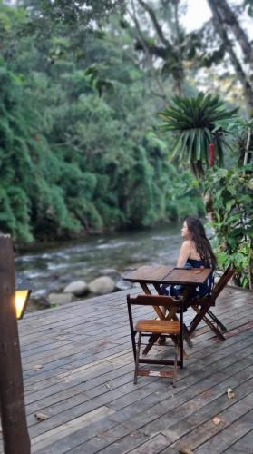 a woman sitting at a table on a wooden deck at Pousada Bosque do Visconde in Visconde De Maua