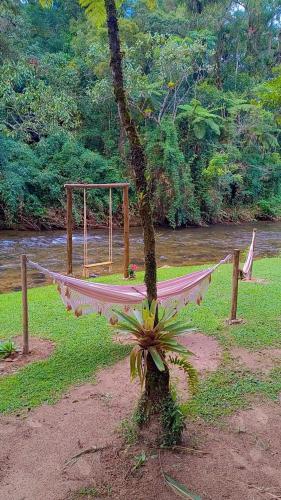 a hammock tied to a tree next to a river at Pousada Bosque do Visconde in Visconde De Maua