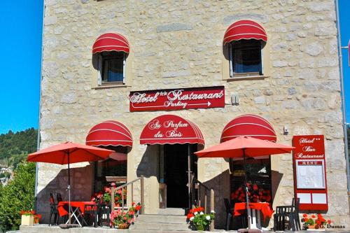 um restaurante com guarda-sóis vermelhos em frente a um edifício em Au Parfum des Bois em Saint-Cirgues-en-Montagne