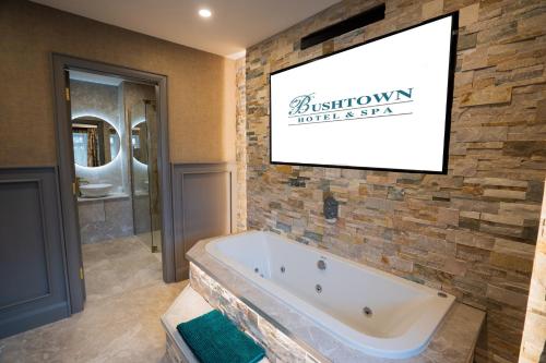 a bathroom with a tub and a television on a wall at Bushtown Hotel & Spa in Coleraine