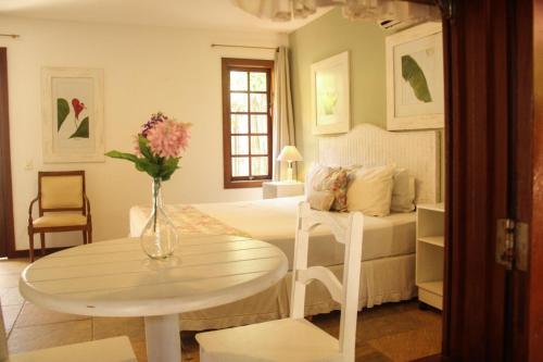 ein Schlafzimmer mit einem Bett und einem Tisch mit einer Blumenvase in der Unterkunft Pousada Blanca Inn in Búzios